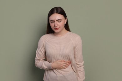 Photo of Young woman suffering from stomach pain on green background