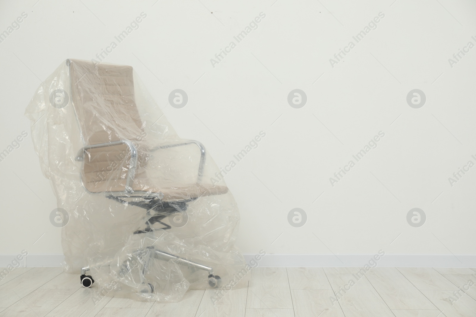 Photo of Modern office chair covered with plastic film near white wall indoors. Space for text