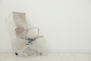 Photo of Modern office chair covered with plastic film near white wall indoors. Space for text