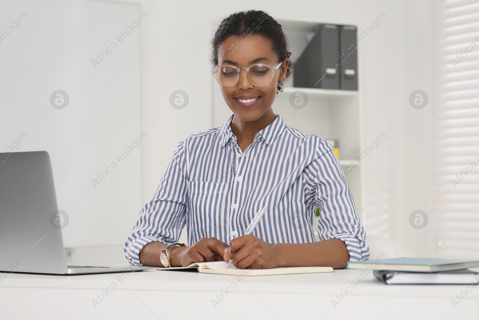 Photo of Smiling African American intern working at white table in office