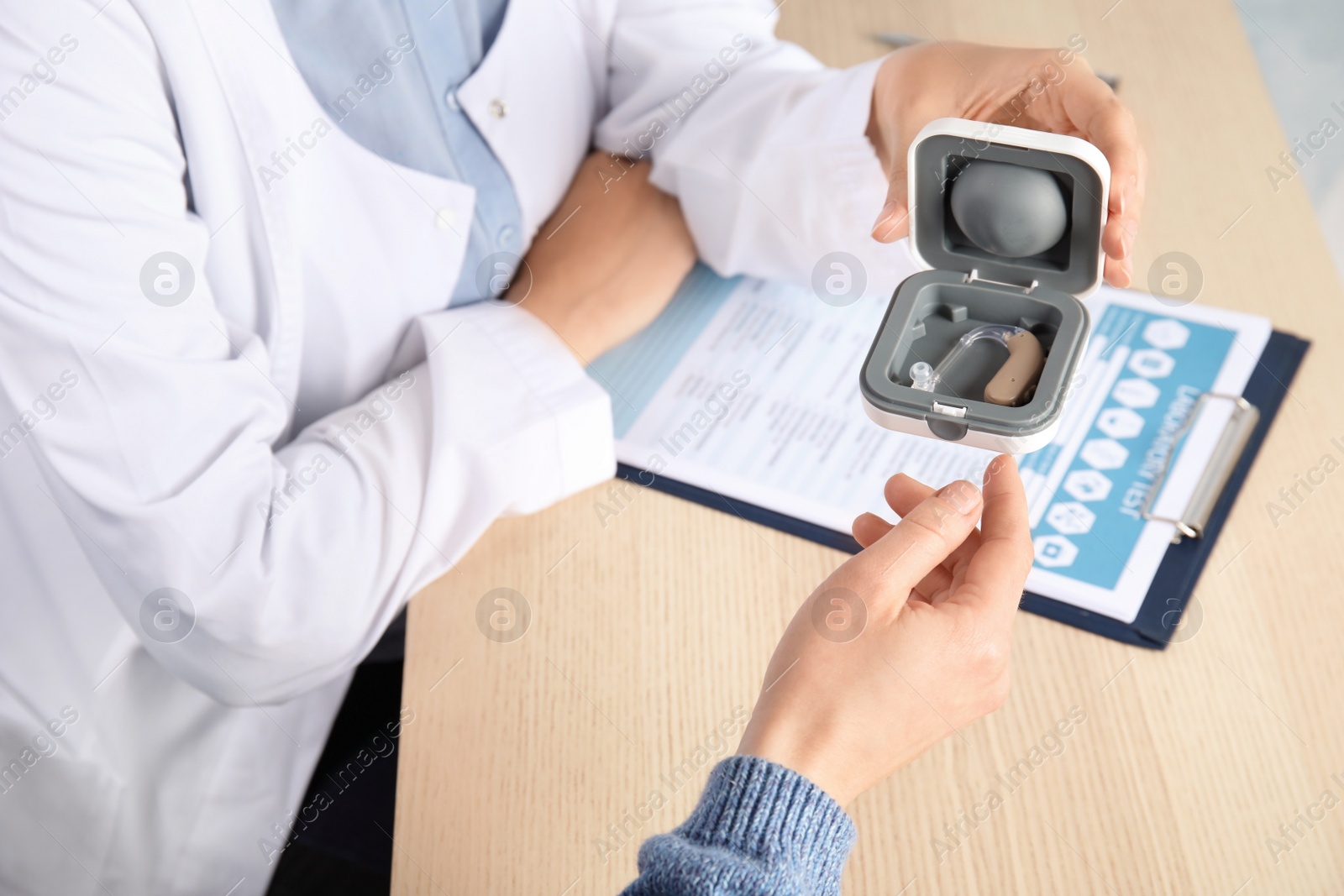 Photo of Doctor giving patient hearing aid at table in clinic, closeup