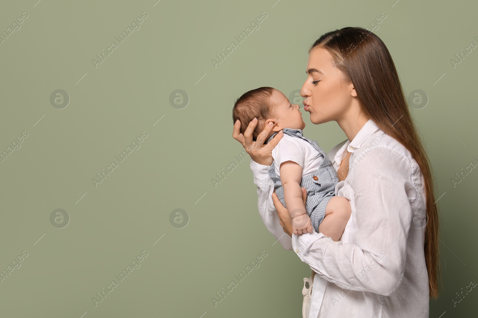 Photo of Mother kissing her cute newborn baby on olive background, space for text