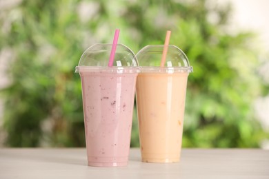 Photo of Plastic cups with different tasty smoothies on wooden table outdoors