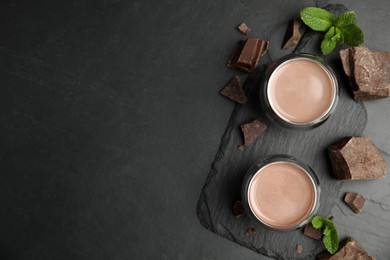 Photo of Glasses of delicious hot chocolate, chunks and fresh mint on black table, flat lay. Space for text