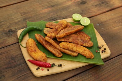 Delicious fried bananas, different peppers and cut limes on wooden table