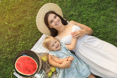 Photo of Mother and her baby daughter resting while having picnic on green grass outdoors, top view