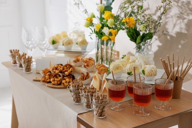 Photo of Delicious treats and glasses of drink on wooden table in room. Sweet buffet
