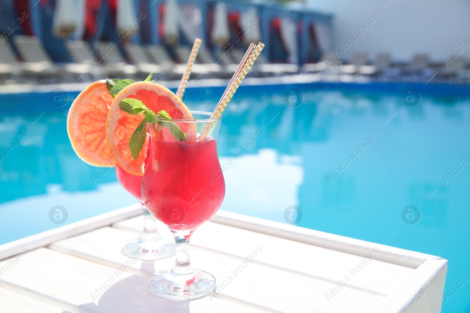 Photo of Refreshing cocktail in glasses near outdoor swimming pool on sunny day. Space for text