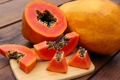 Photo of Ripe cut and whole papaya fruits on wooden table, closeup