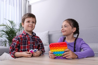 Photo of Little children playing with pop it and simple dimple fidget toys at wooden table in living room