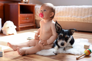 Photo of Adorable baby with pacifier and cute dog on faux fur rug at home