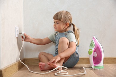 Photo of Little child playing with electrical socket and iron plug at home. Dangerous situation