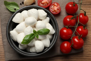 Photo of Delicious mozzarella balls, tomatoes and basil leaves on wooden table, flat lay