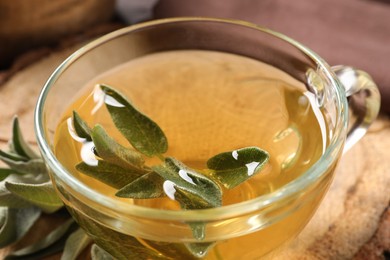 Photo of Cup of aromatic sage tea with fresh leaves on table, closeup