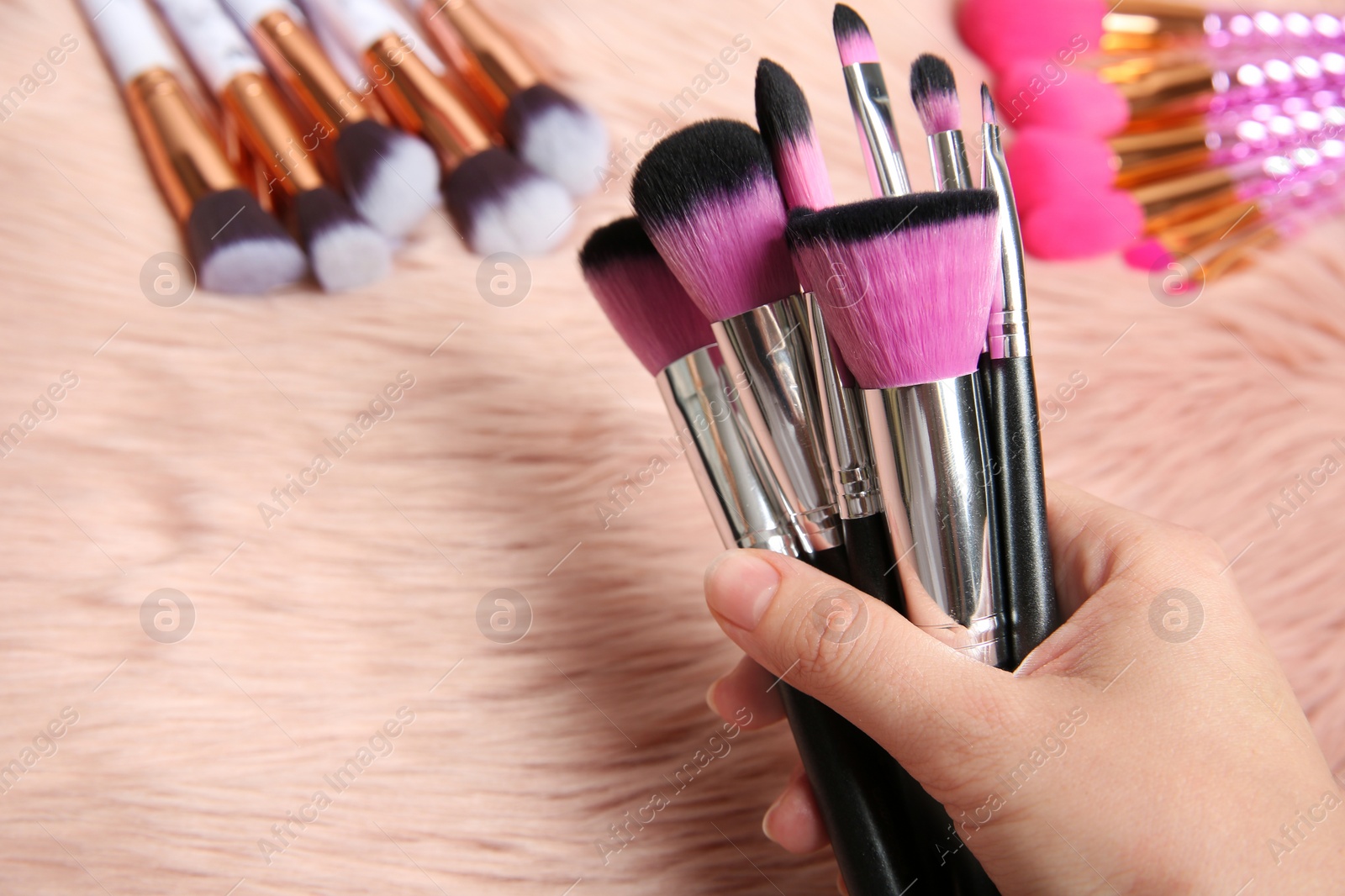 Photo of Woman holding makeup brushes over furry fabric, closeup view. Space for text