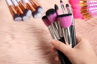 Woman holding makeup brushes over furry fabric, closeup view. Space for text