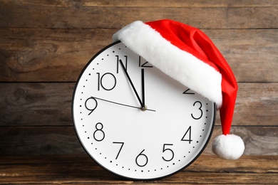 Photo of Clock with Santa hat showing five minutes until midnight on wooden background. New Year countdown