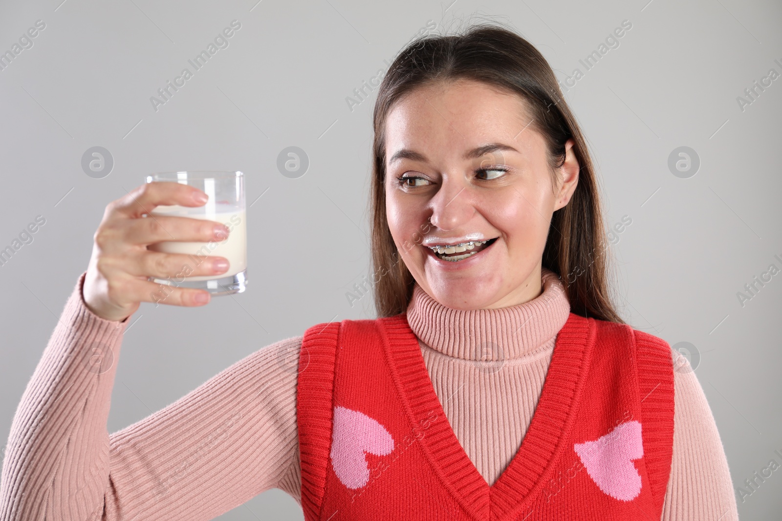 Photo of Happy woman with milk mustache holding glass of drink on light grey background