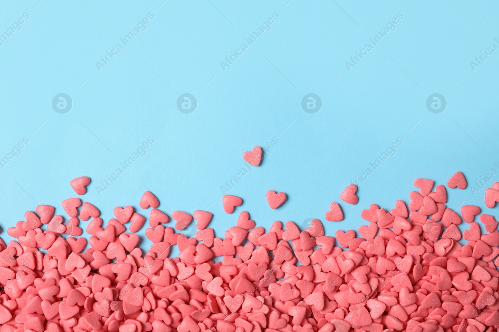 Photo of Bright heart shaped sprinkles on light blue background, flat lay. Space for text