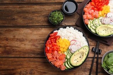 Photo of Delicious poke bowls with salmon and vegetables served on wooden table, flat lay. Space for text