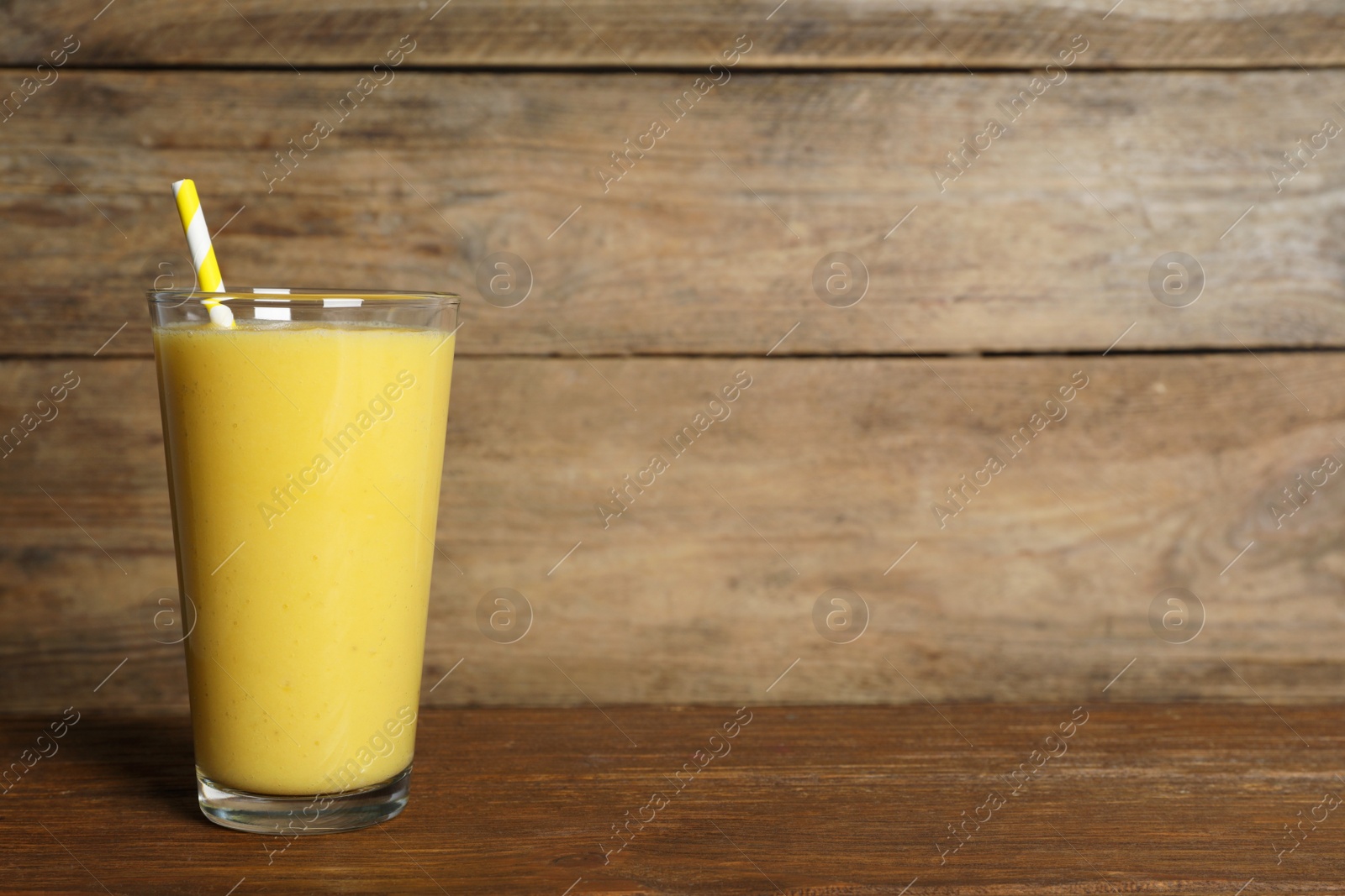 Photo of Glass of tasty smoothie with straw on wooden table. Space for text