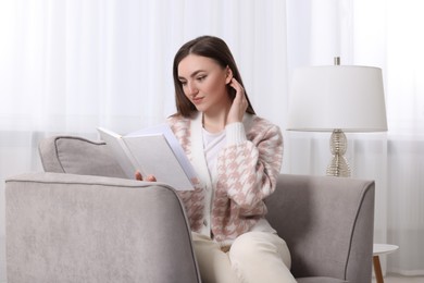 Woman reading book on armchair near window at home