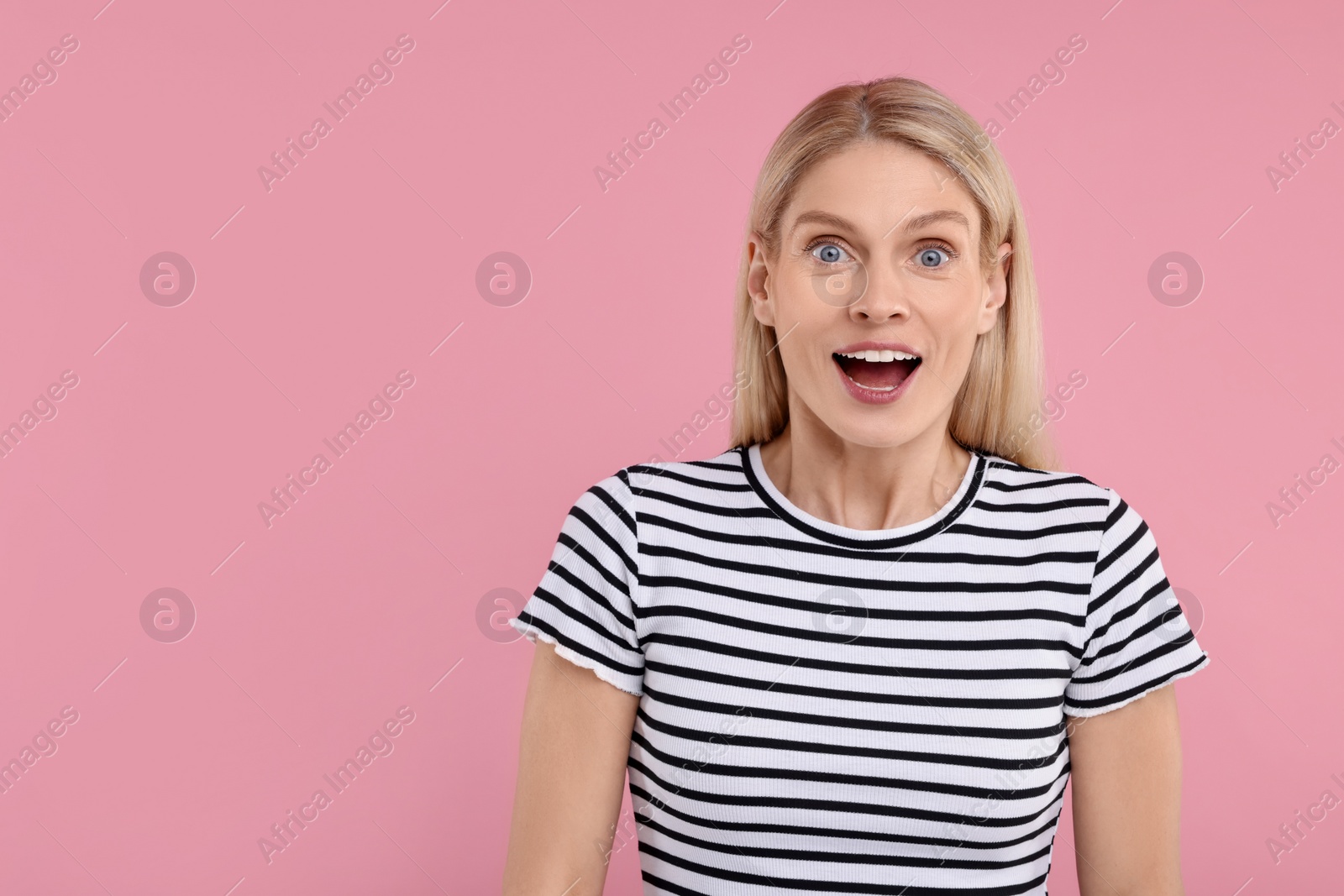 Photo of Portrait of surprised woman on pink background, space for text