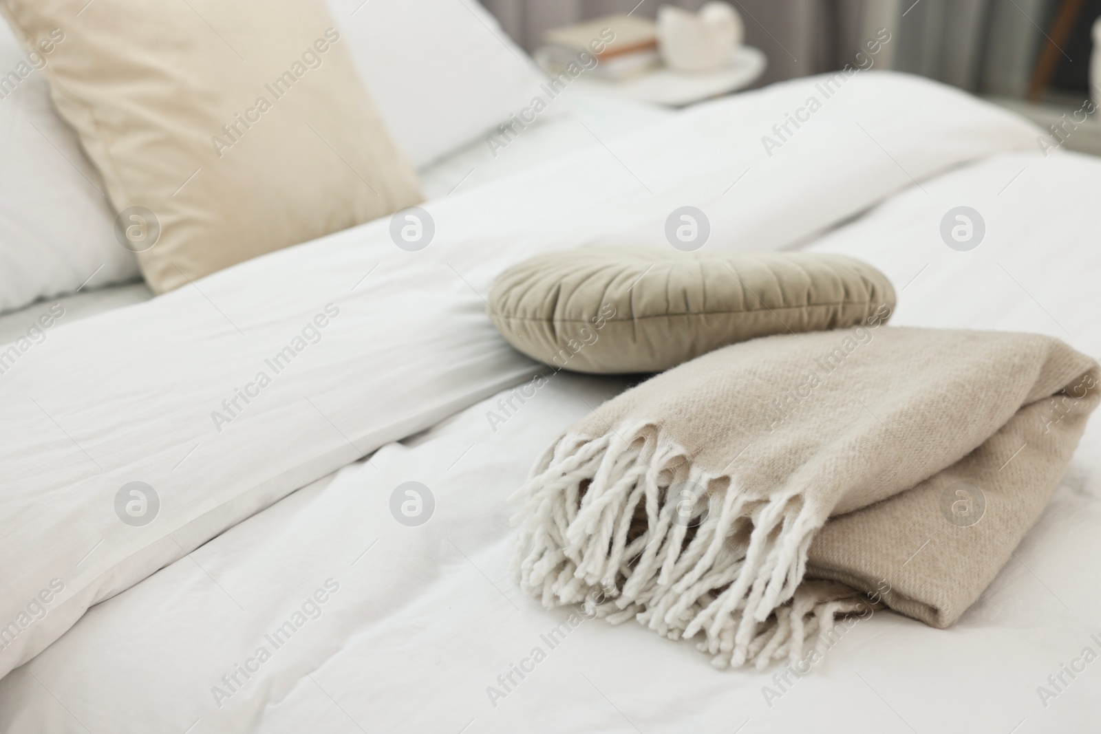 Photo of Soft beige plaid and pillow on bed in room