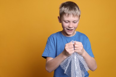 Photo of Happy boy popping bubble wrap on yellow background, space for text. Stress relief
