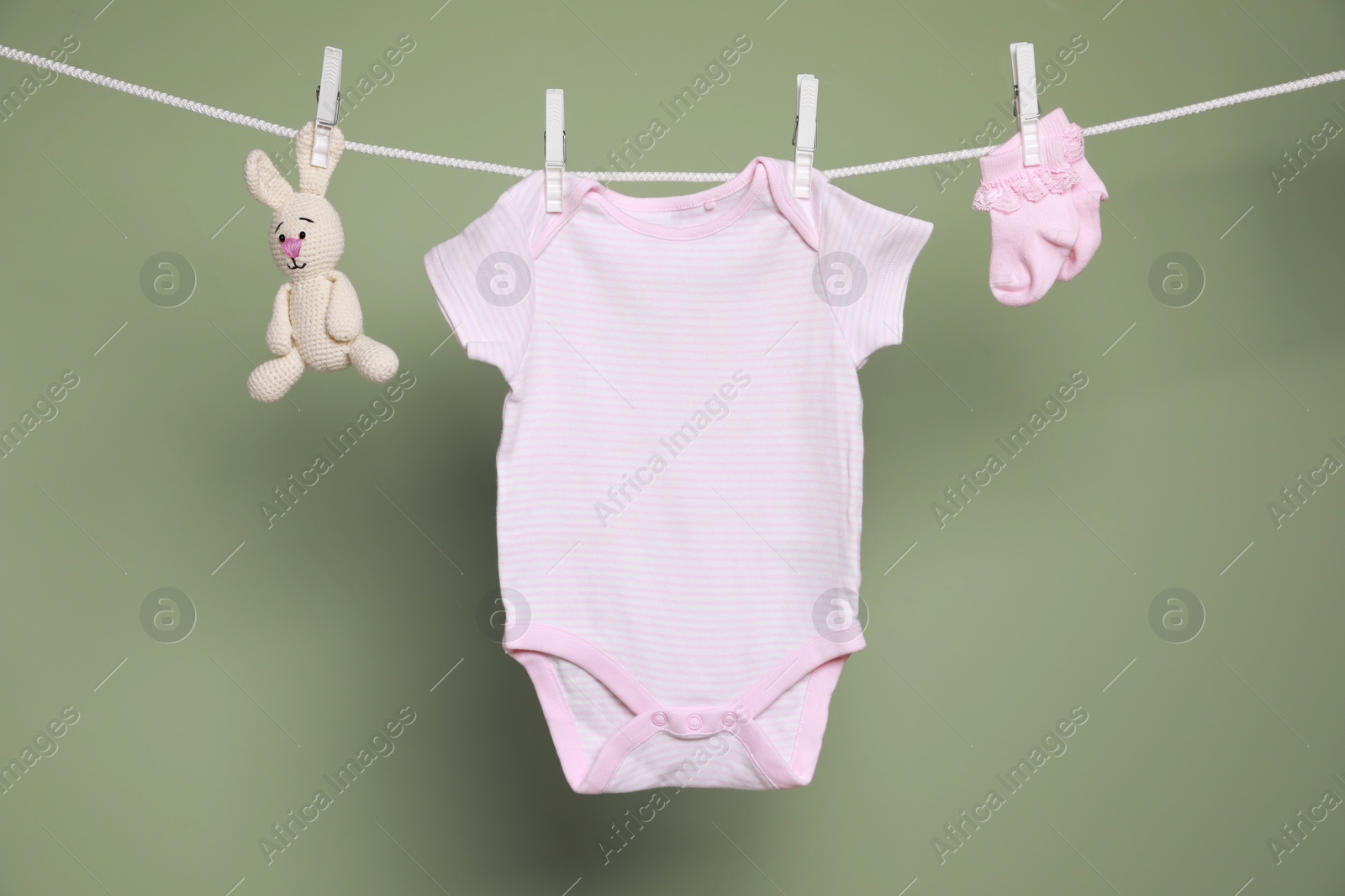 Photo of Cute small baby clothes and toy hanging on washing line against green background