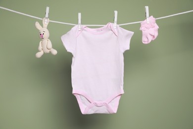 Cute small baby clothes and toy hanging on washing line against green background