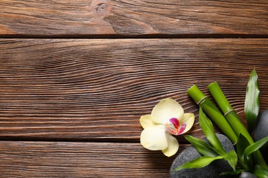 Photo of Spa stones, orchid flower and bamboo stems on wooden background, flat lay. Space for text