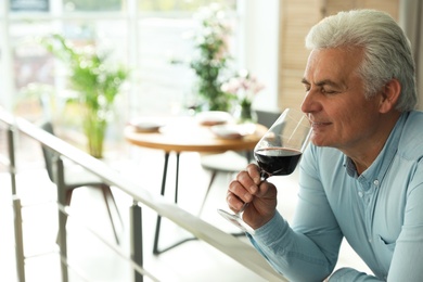 Photo of Senior man with glass of wine in restaurant. Space for text