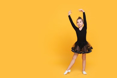 Photo of Cute little girl in black dress dancing on yellow background. Space for text