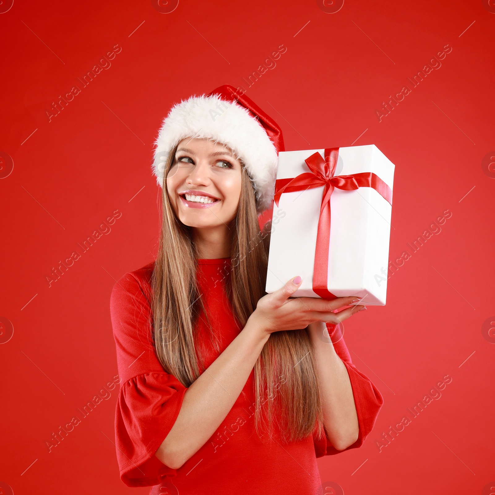 Photo of Happy young woman in Santa hat with Christmas gift on red background