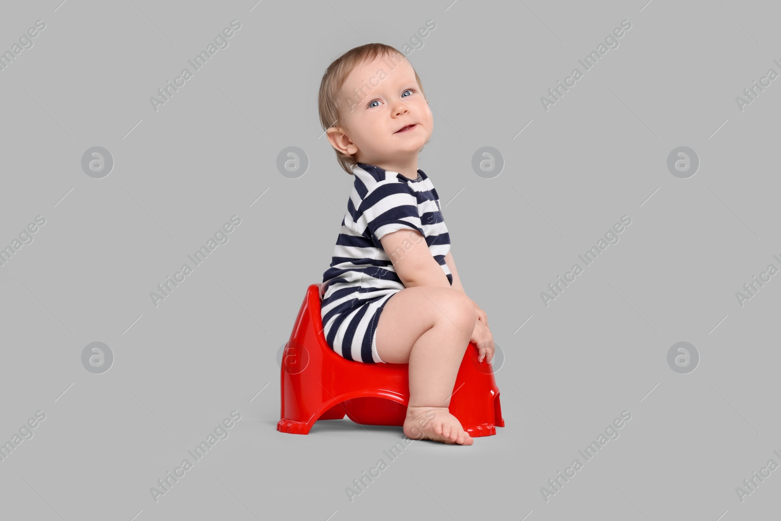 Photo of Little child sitting on baby potty against light grey background