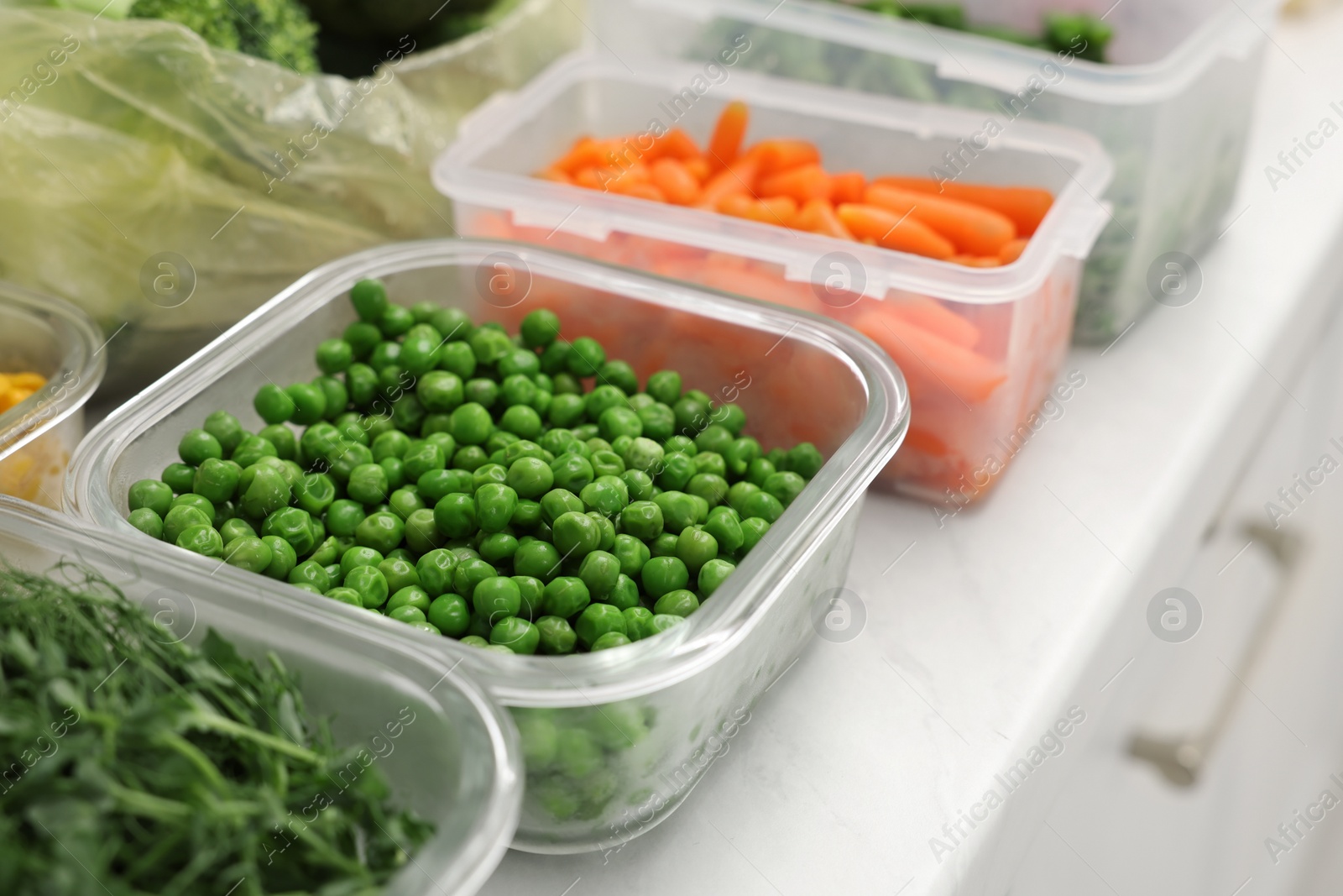 Photo of Plastic and glass containers with different fresh products on white countertop, closeup