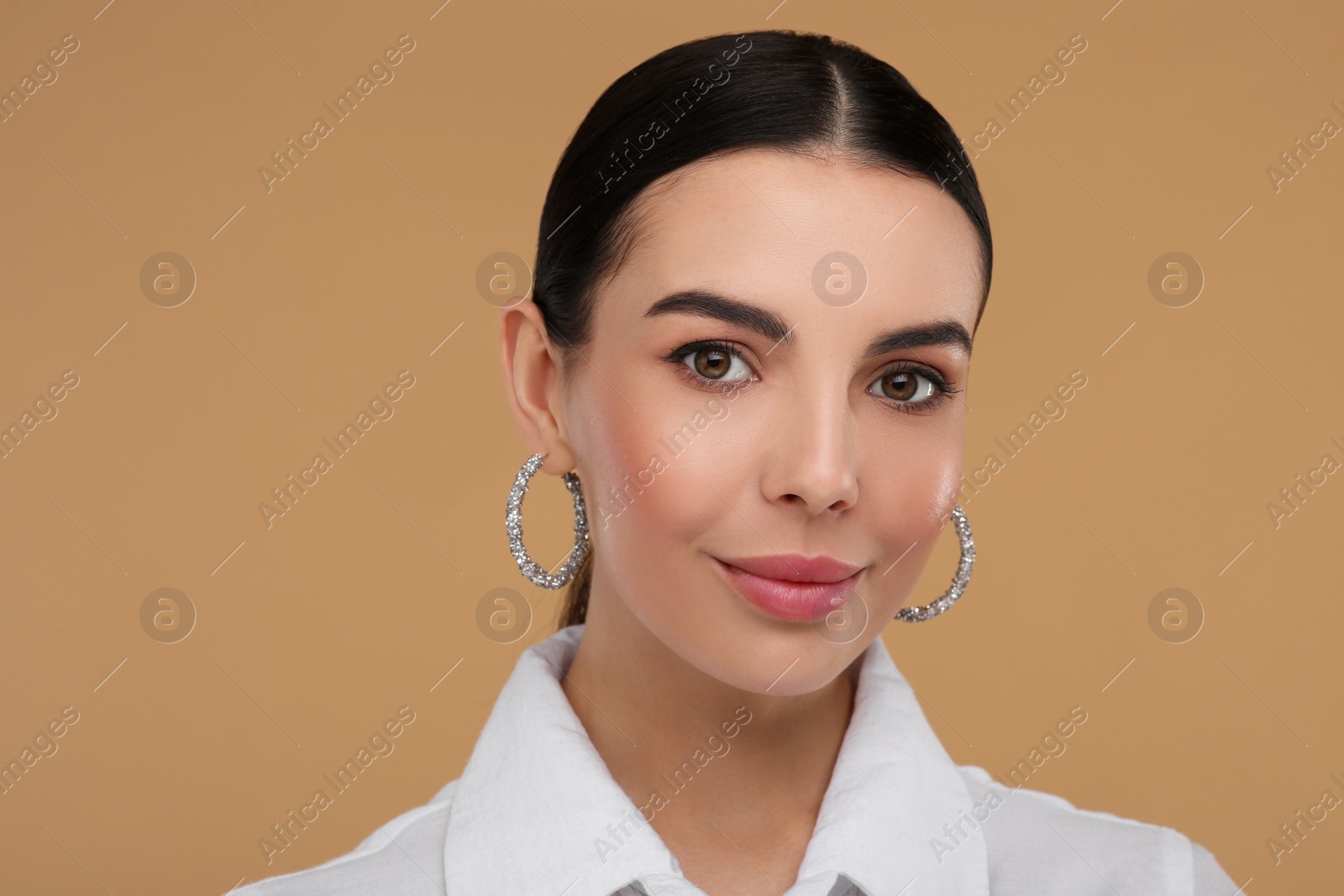 Photo of Beautiful young woman with elegant earrings on beige background