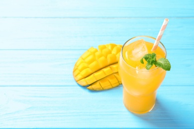 Photo of Fresh mango drink and cut fruit on blue wooden table. Space for text