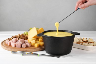 Photo of Woman dipping piece of ham into fondue pot with tasty melted cheese at white wooden table, closeup