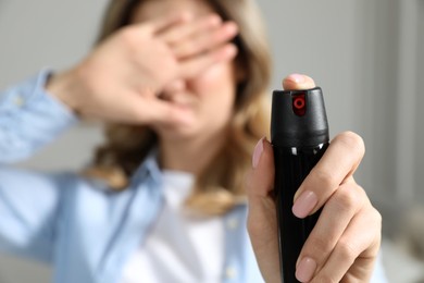 Photo of Young woman covering eyes with hand and using pepper spray at home