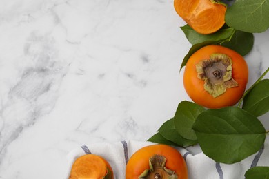 Photo of Whole and cut delicious ripe juicy persimmons with green leaves on white marble table, flat lay. Space for text