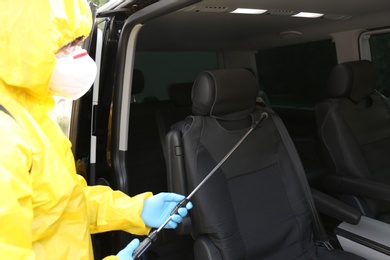 Photo of Person in protective suit disinfecting car with sprayer. Preventive measure during coronavirus pandemic