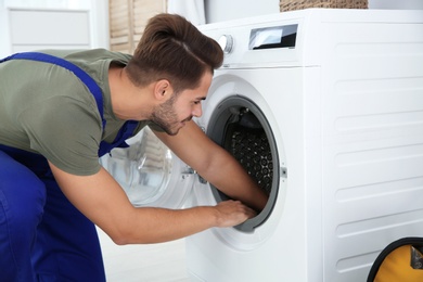 Photo of Young handyman fixing washing machine at home. Laundry day