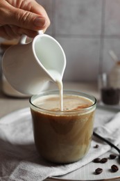 Photo of Woman pouring milk into cup with coffee at table, closeup