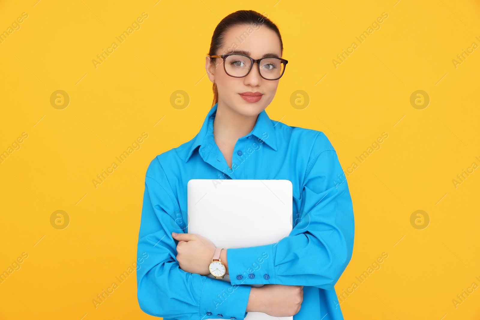 Photo of Young female intern with laptop on yellow background