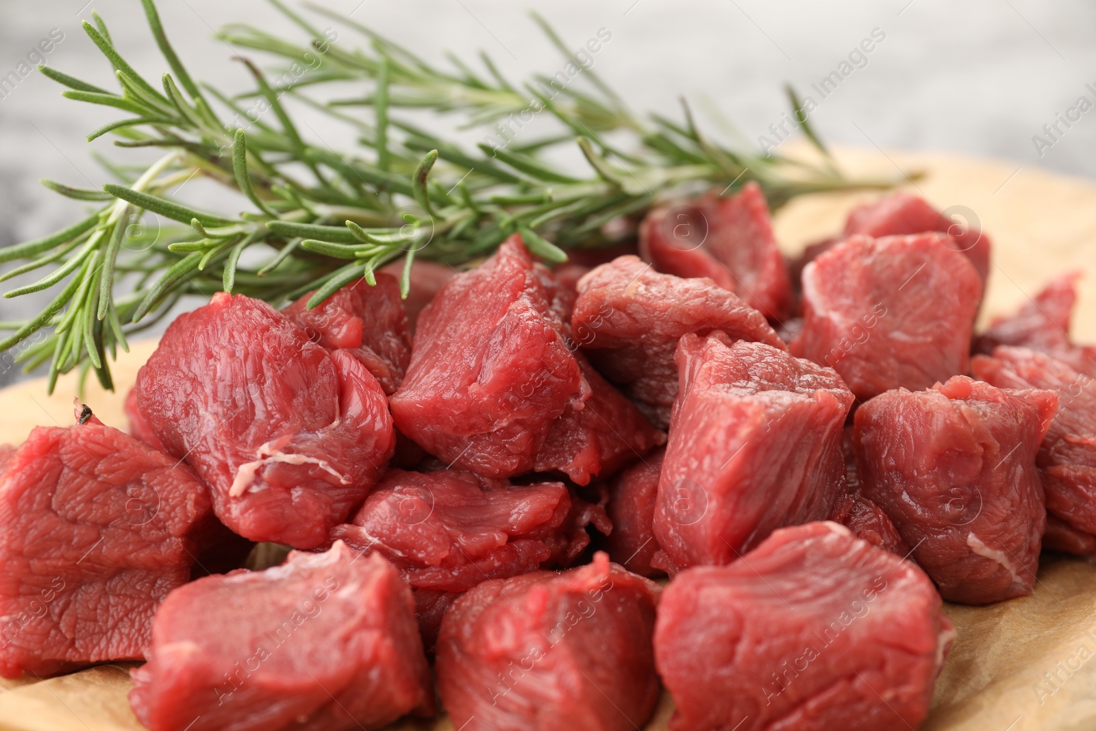 Photo of Pieces of raw beef meat and rosemary on parchment, closeup