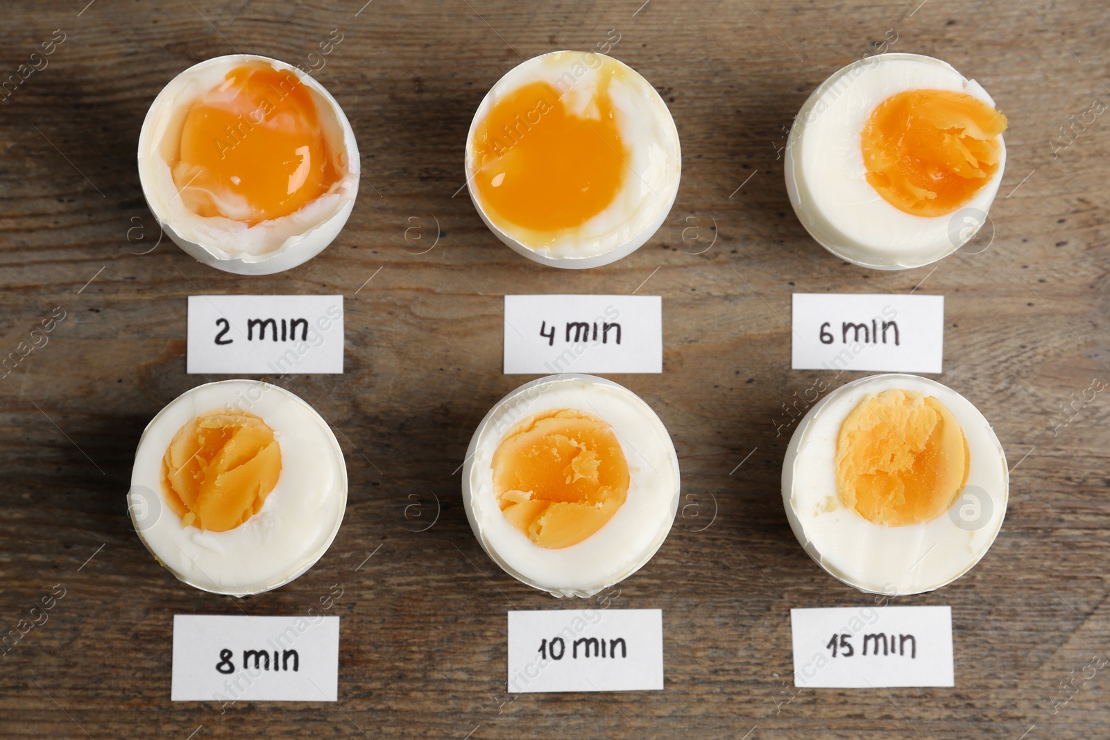 Photo of Different cooking time and readiness stages of boiled chicken eggs on wooden table, flat lay