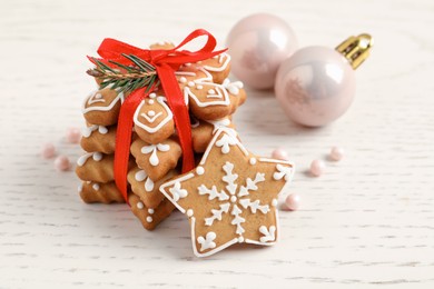 Photo of Tasty Christmas cookies tied with red ribbon and festive decor on beige wooden table, closeup