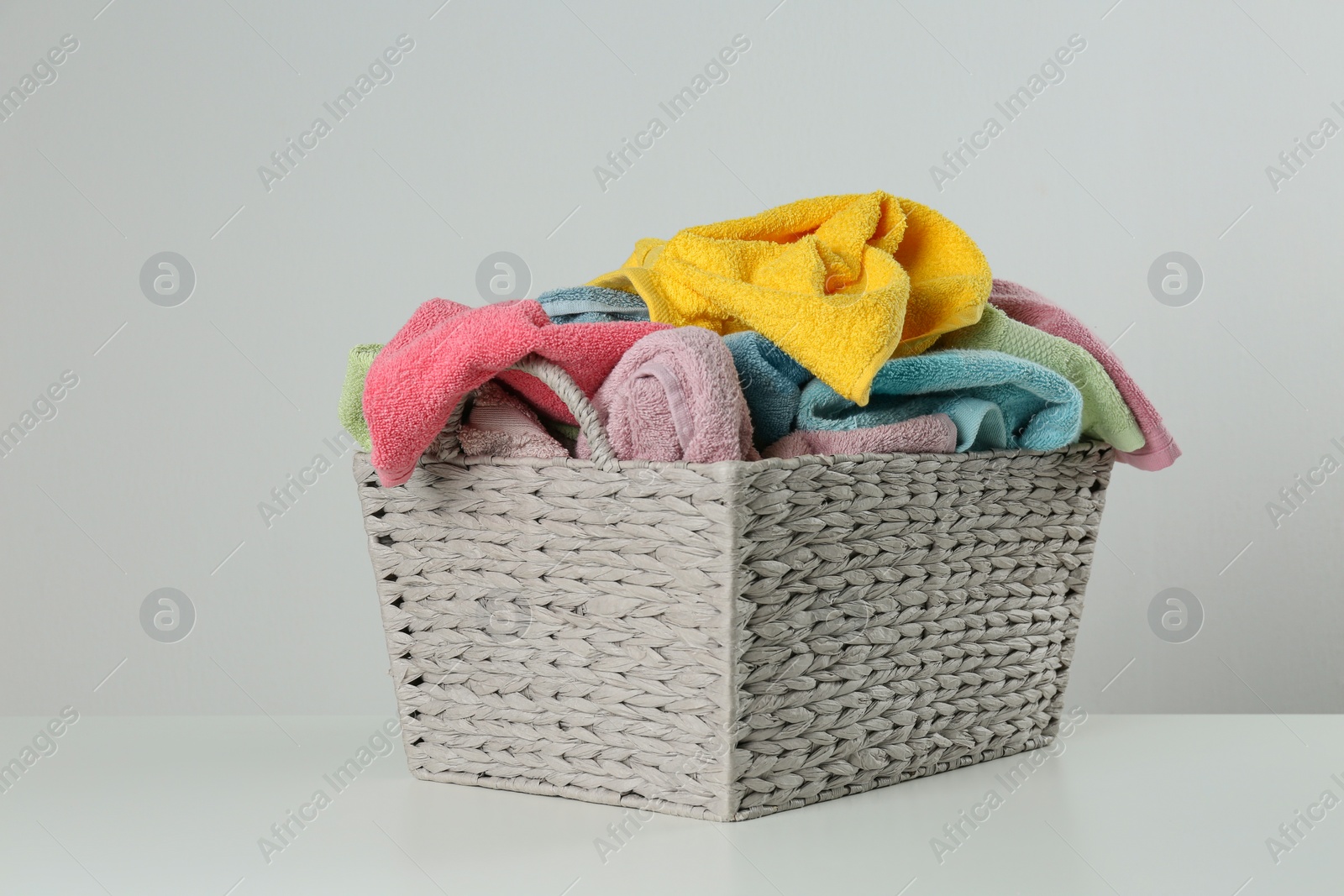 Photo of Wicker laundry basket with towels on light background